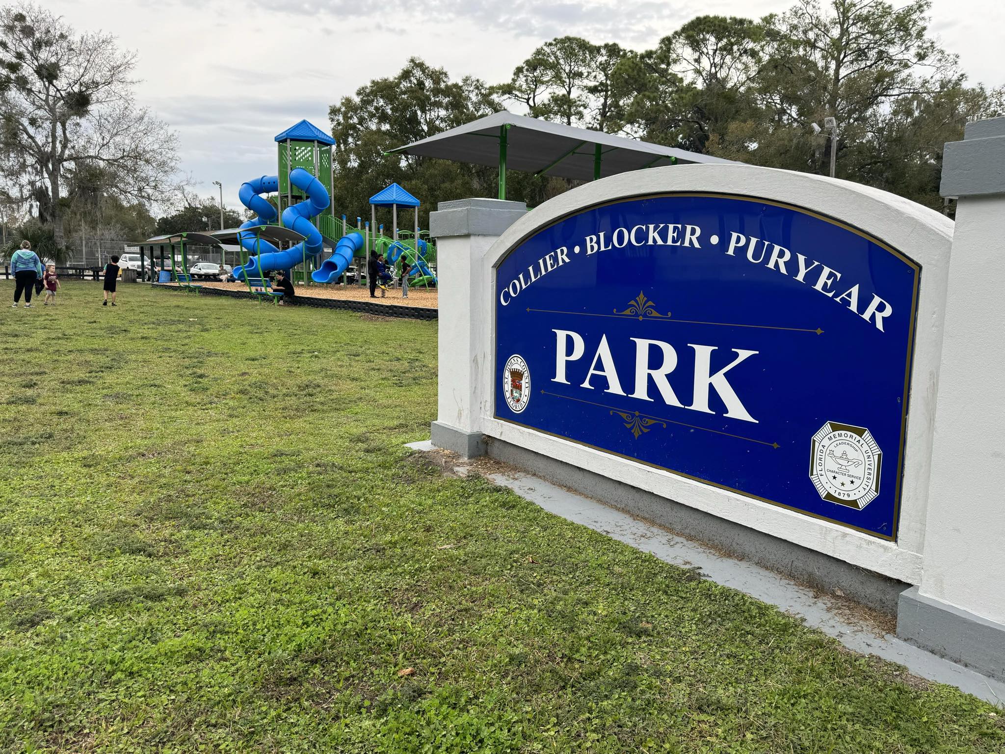 Sign reads "Collier-Blocker-Puryear Park" in front of a playground surrounded by little children.