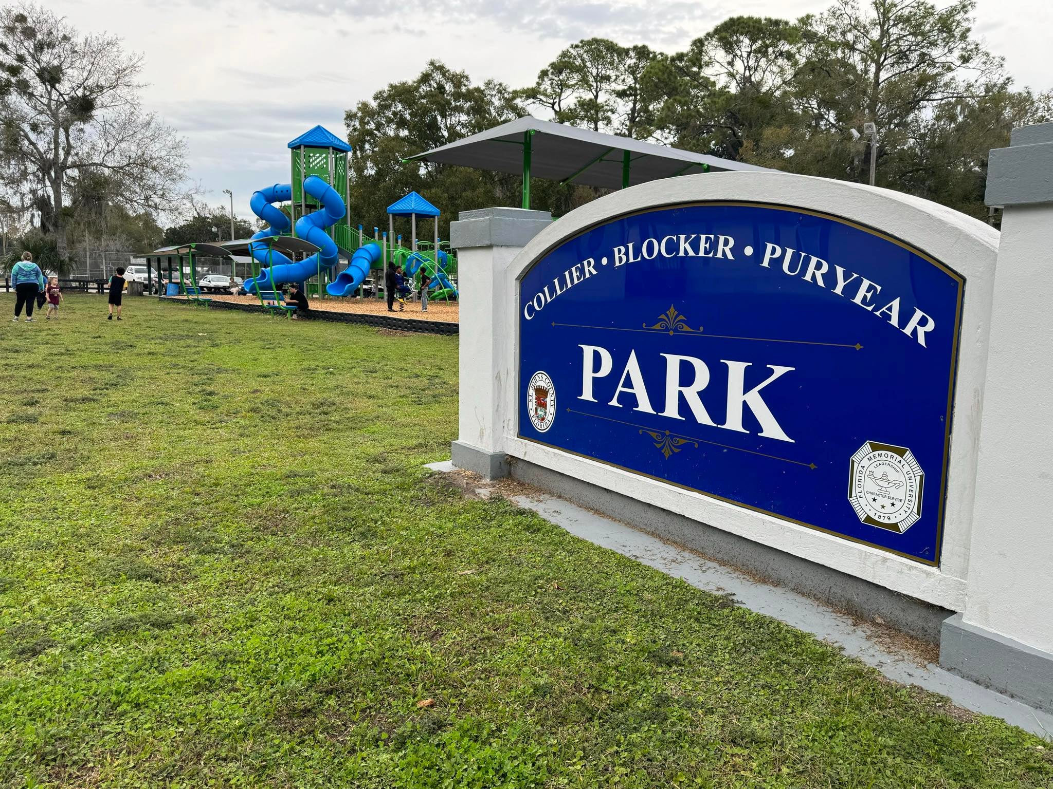 Sign reads "Collier-Blocker-Puryear Park" in front of a playground surrounded by little children.