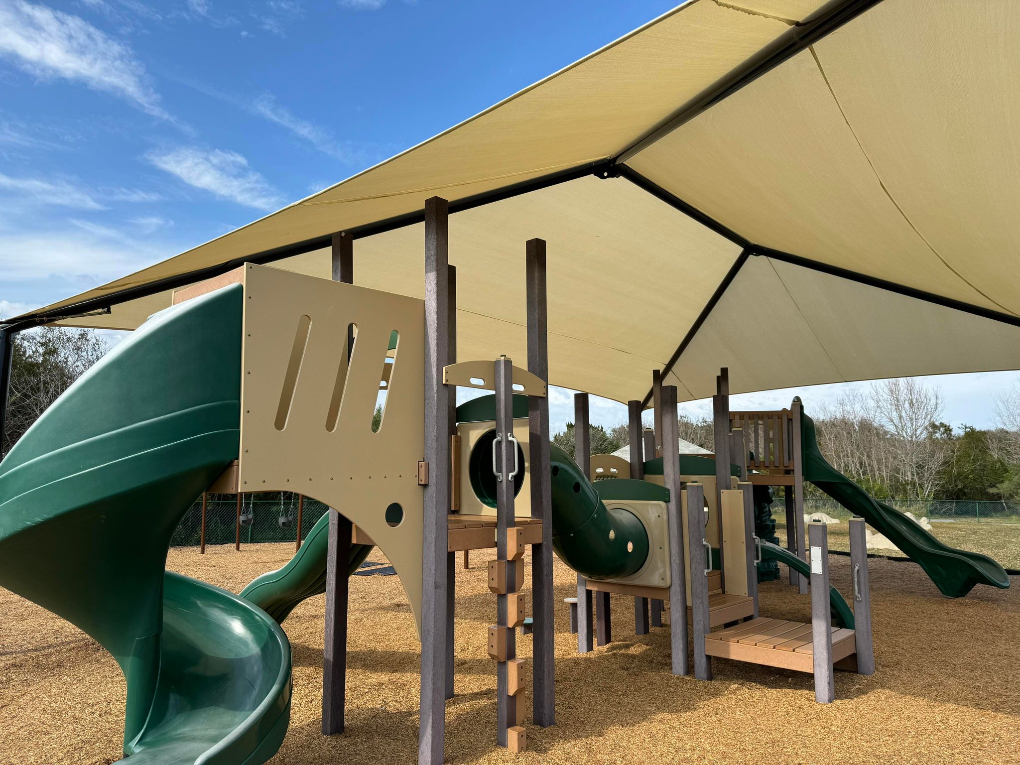 A playground structure with a slide underneath a canvas shade structure.