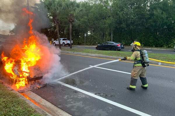 firefighter spraying water on burning vehicle
