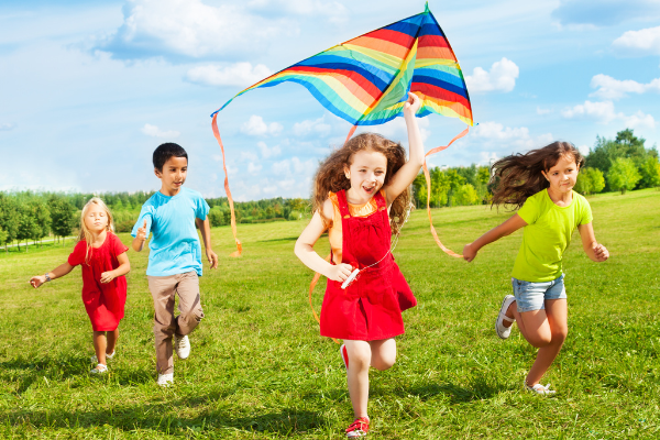 Children running through a sunny grass field with a kite.