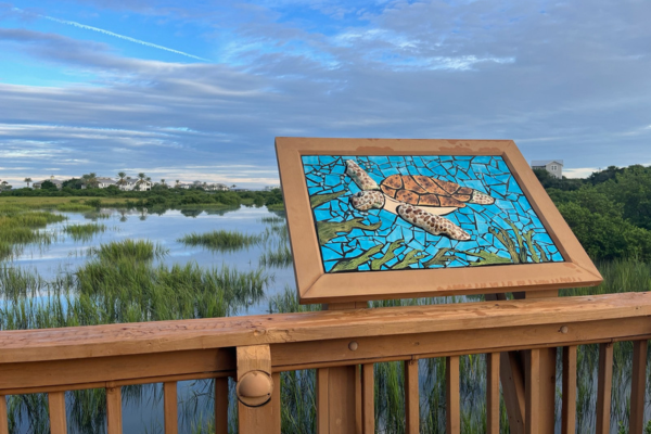 a sea turtle mosaic art piece with a view of the marsh behind it