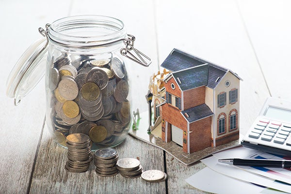 Jar full of coins next to a miniature house and calculator