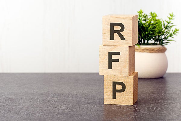 Wooden blocks spelling RFP with green plant in background