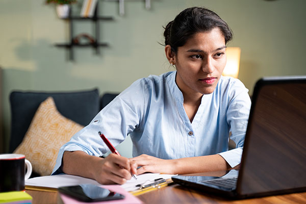 Young business woman writing down notes by looking at her laptop
