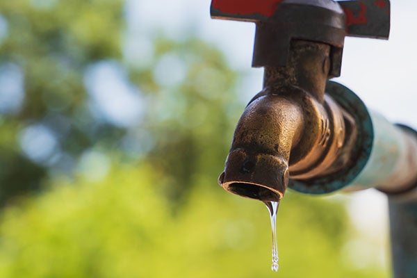 Old metal water tap with water drop as natural green background