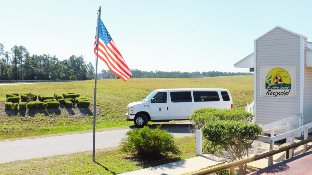 Van parked outside a scale house with an american flag and shrubs pruned to say Solid Waste