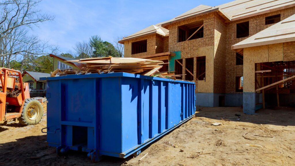 blue dumpster full of construction debris in front of house being built