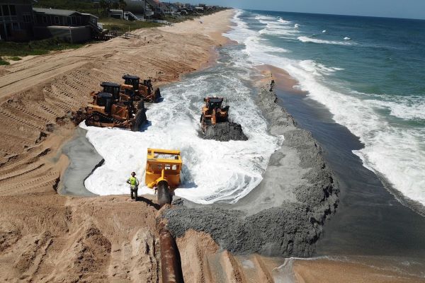 Sand being pumped onto the beach and being formed into new dune/berm by heavy machinery.