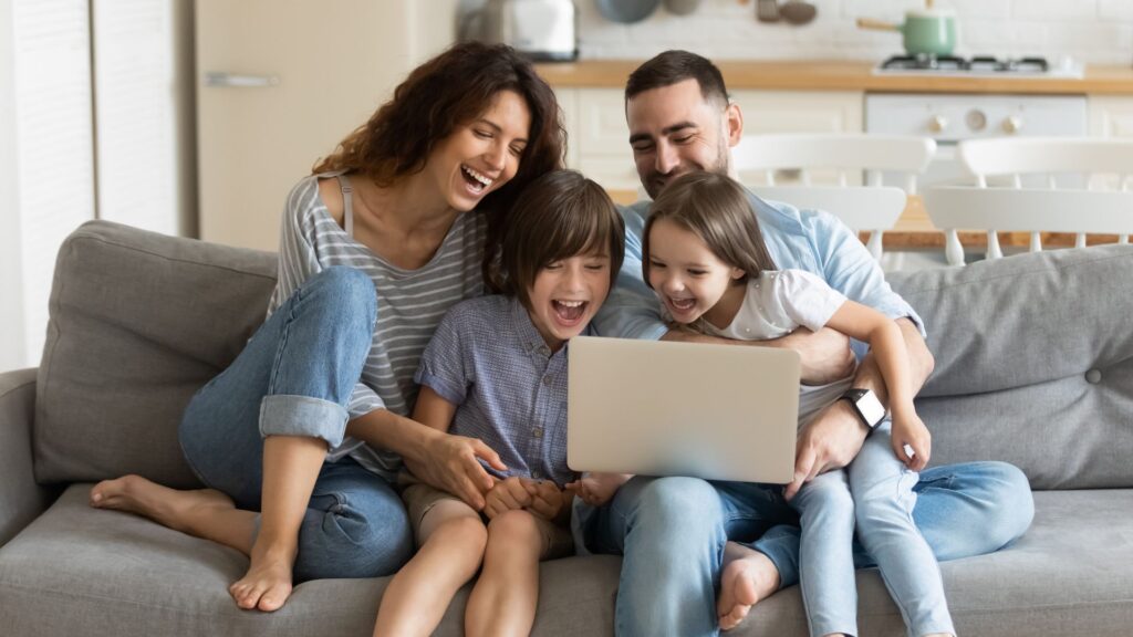 family on a couch sharing a laptop computer and laughing
