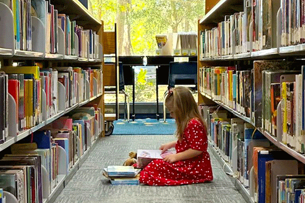 young child sitting on library floor reading books