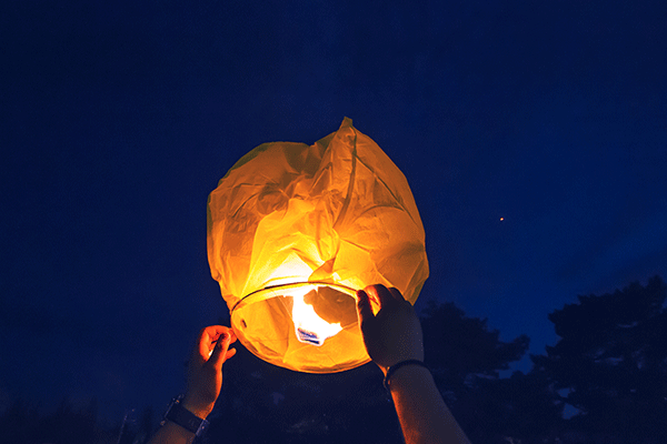 sky lantern being launched into the night sky by human hands