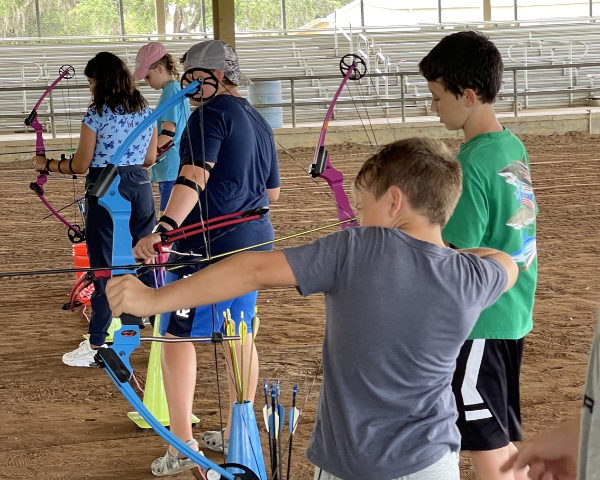 Five children lined up aiming bows and arrows at targets .