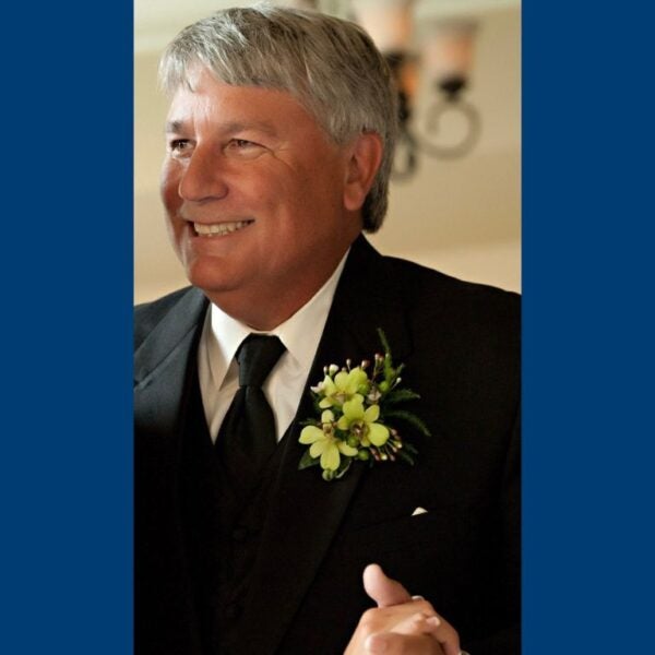 A smiling older man wearing a tuxedo with a boutonniere.