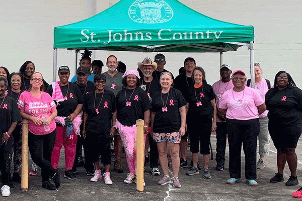 A large group of people in pink and black walking attire outside by a tent.