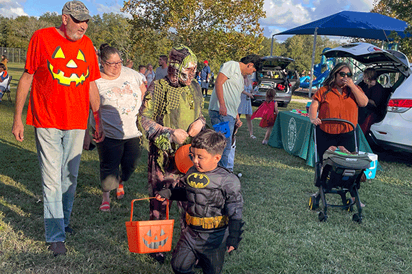 Children and adults go trunk-or-treating in a public park.
