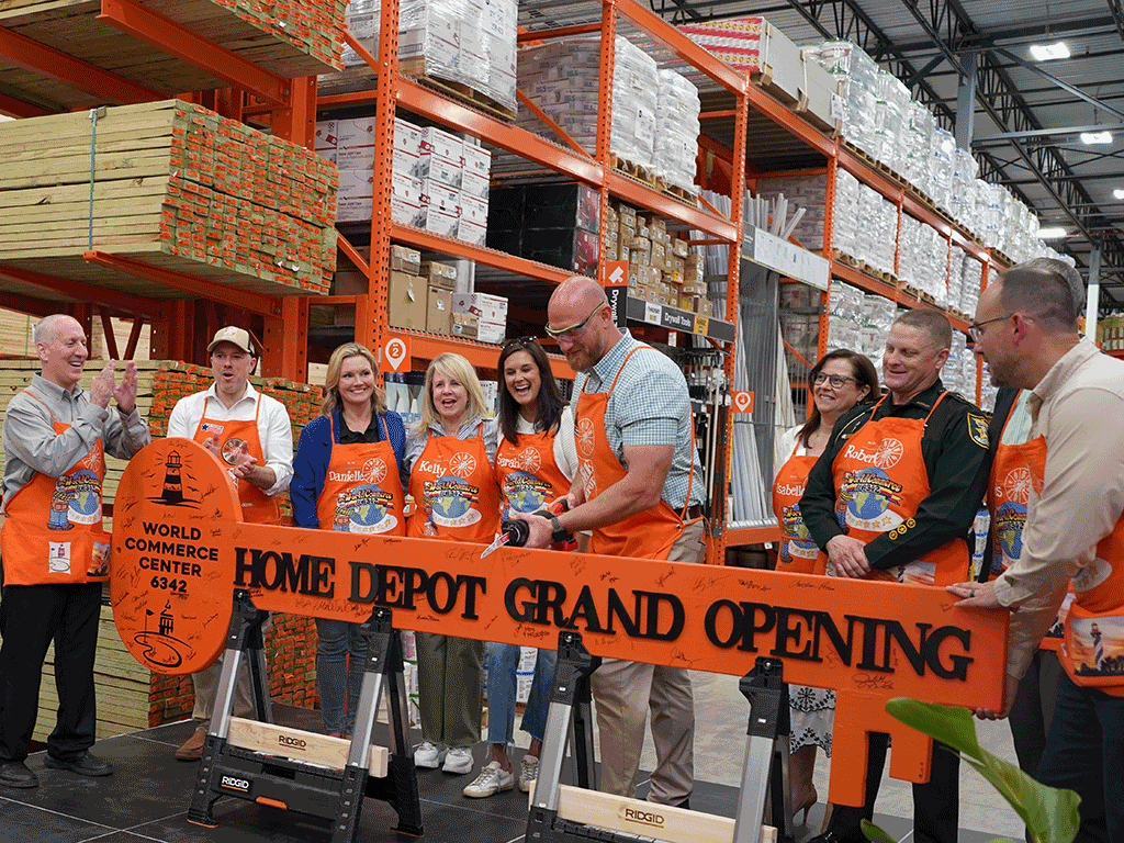 Commissioner Arnold stands with others as the Home Depot Grand Opening board is cut with a power tool.