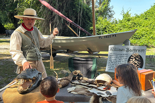 A man in an 18th century costume speaks to children at an outdoor event