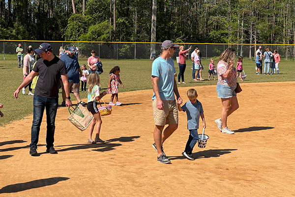 A large crowd of parents and children with baskets search for Easter eggs on a baseball field