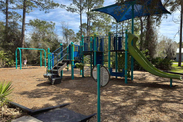 A shaded playground with a young girl on a swingset.