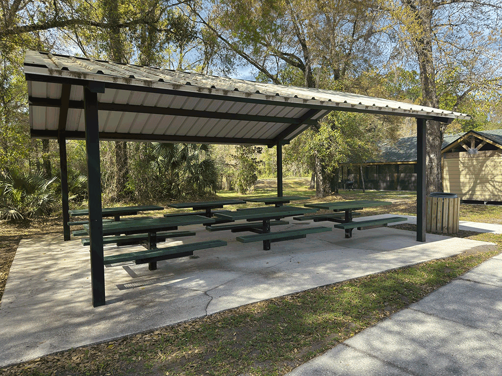 Six picnic tables under an outdoor covering.