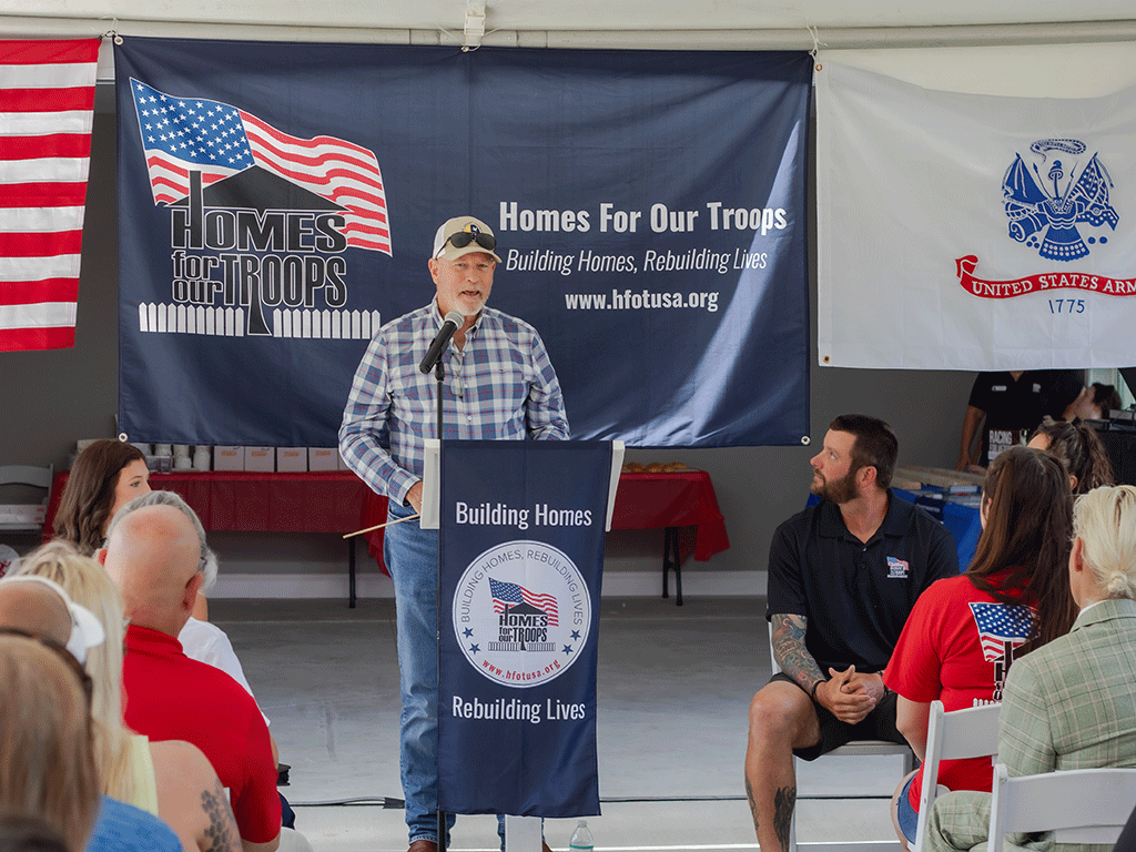 Commissioner Murphy speaks at a podium in front of a sign that says, "Home for our Troops, building homes, rebuilding lives."
