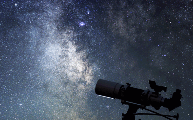A telescope pointed upward at a starry night sky.