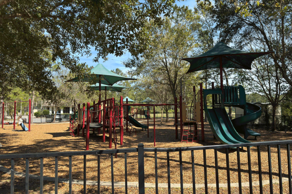 A large playground with shaded play structures surrounded by trees.