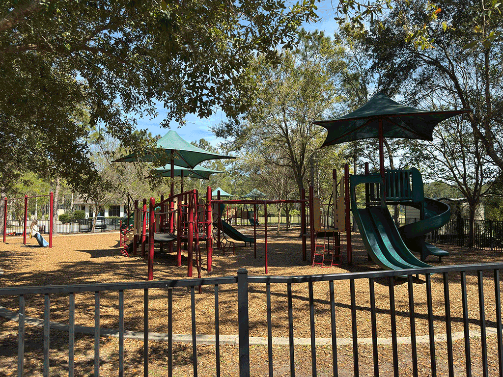 A large playground with shaded play structures surrounded by trees.