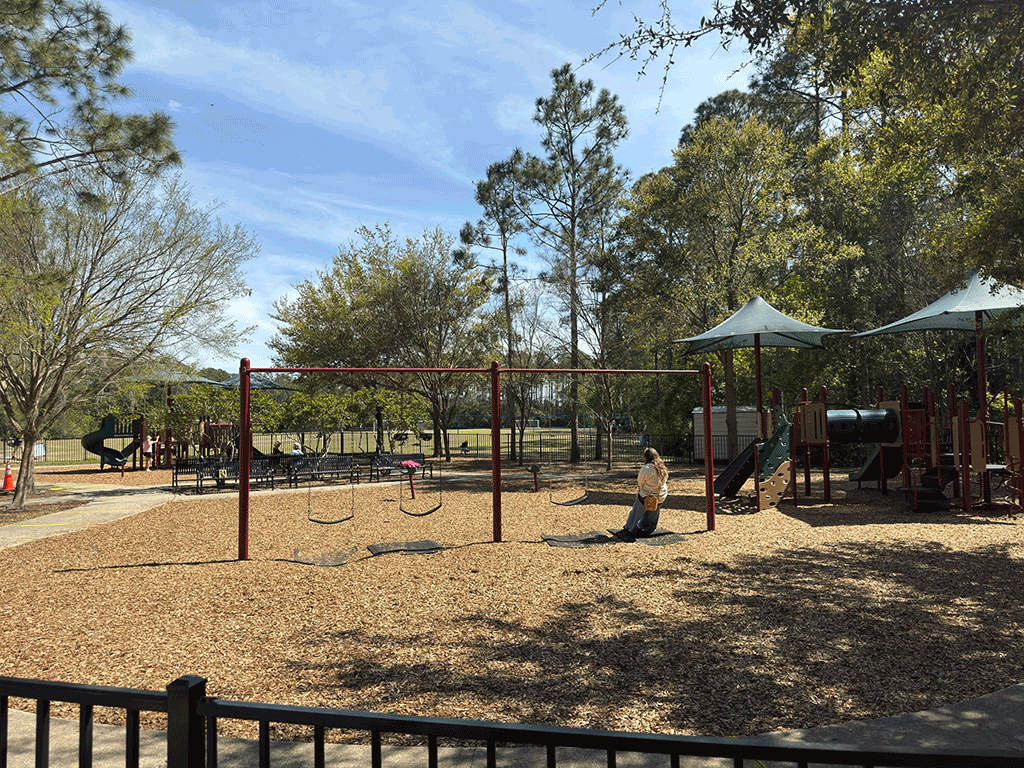 Adults on benches and swings watch children on a playground.