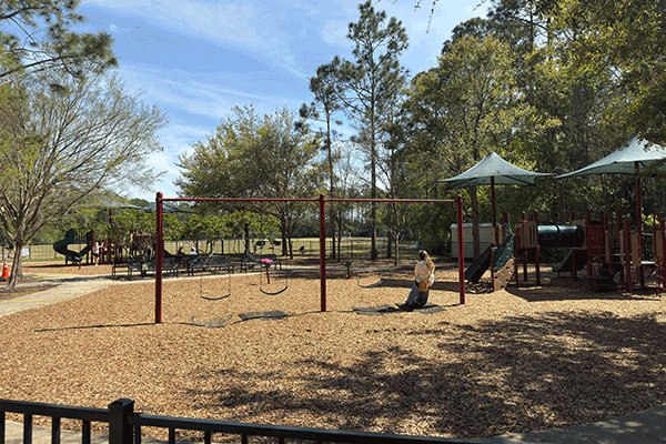 Adults on benches and swings watch children on a playground.