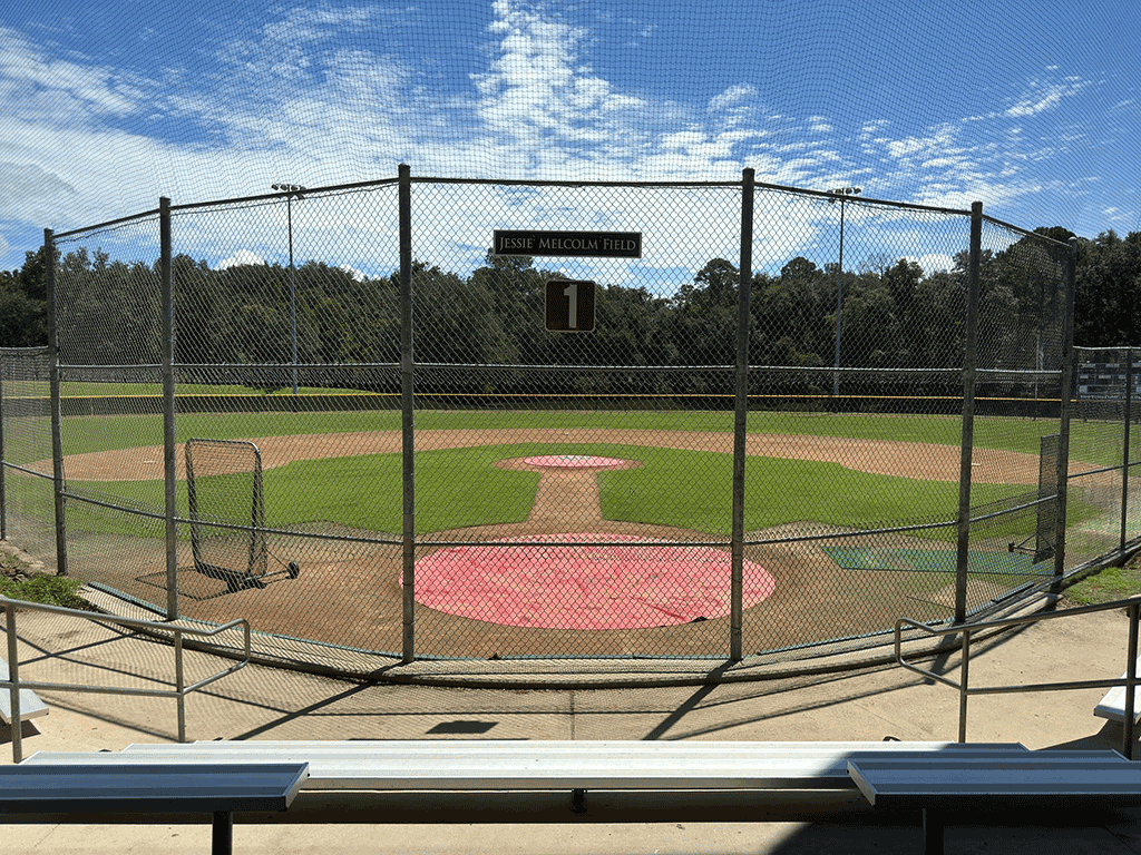 A baseball field behind a fence, as seen from bleachers on the other side.