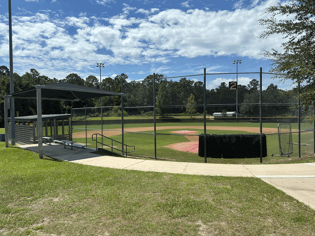A fenced-in baseball field with shaded bleachers and a dugout.