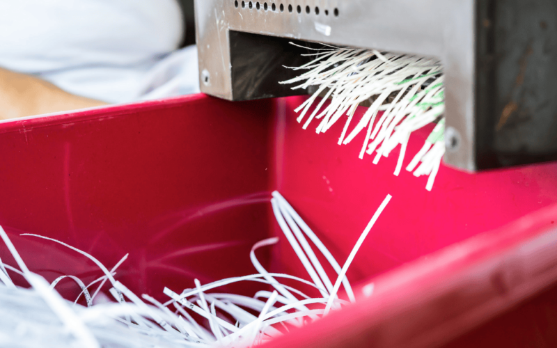 A machine shredding paper as it falls into a red bin.