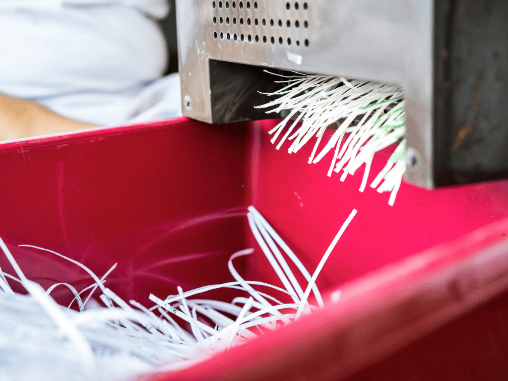 A machine shredding paper as it falls into a red bin.