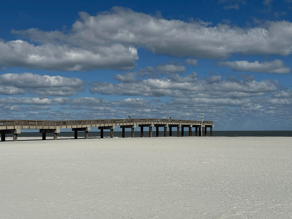 A pier stretches toward the ocean across a wide sandy beach.