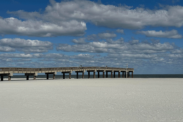 A pier stretches toward the ocean across a wide sandy beach.