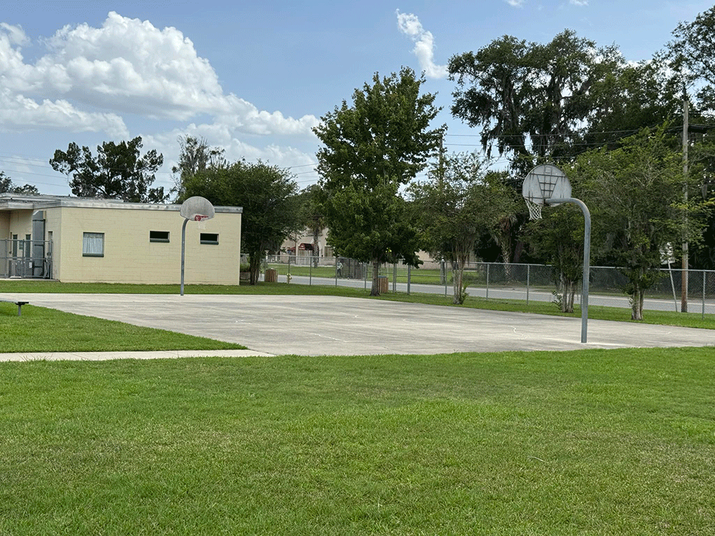 An outdoor concrete basketball court with two hoops.