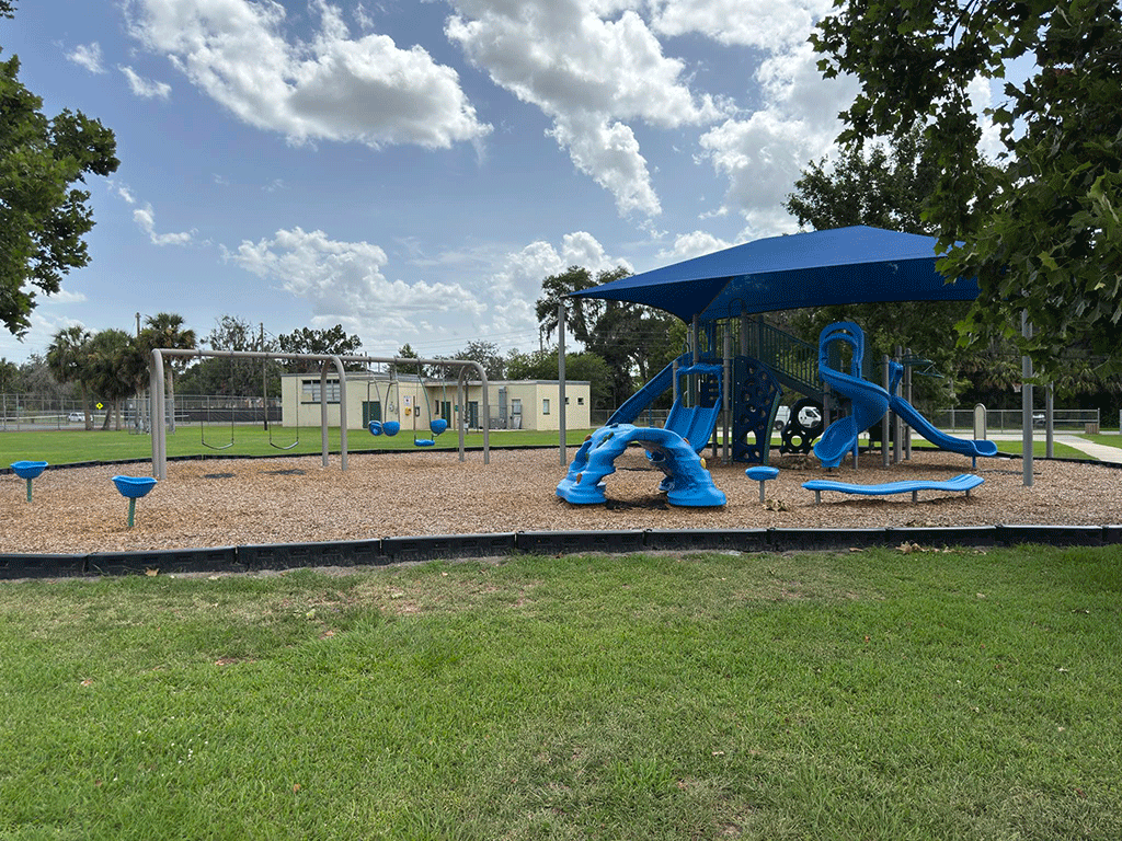 A park playground with a swing set, climbing structures, and a covered play area with slides