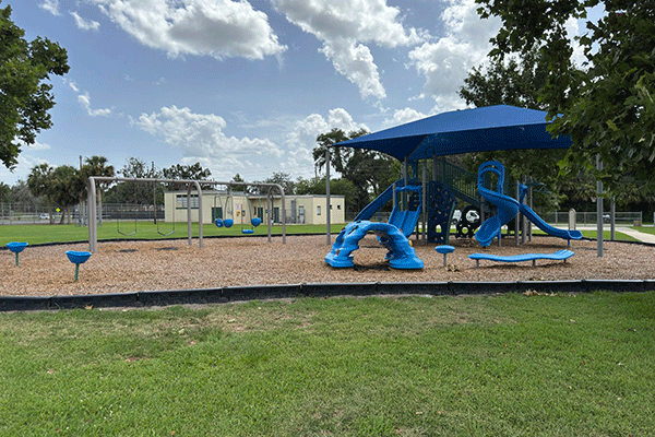 A park playground with a swing set, climbing structures, and a covered play area with slides