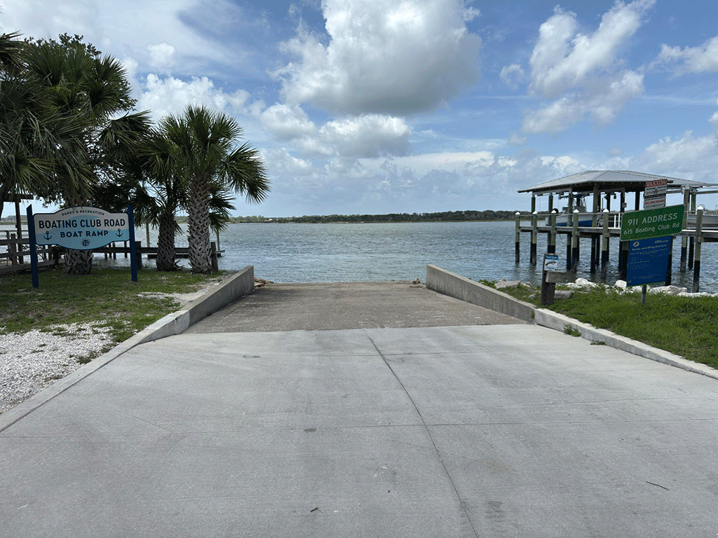 A concrete boat ramp into the Intracoastal, with boat docks on either side and a sign marking it as the Boating Club Road Boat Ramp.