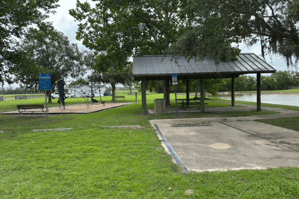 A playground and a covered picnic table by a pond.