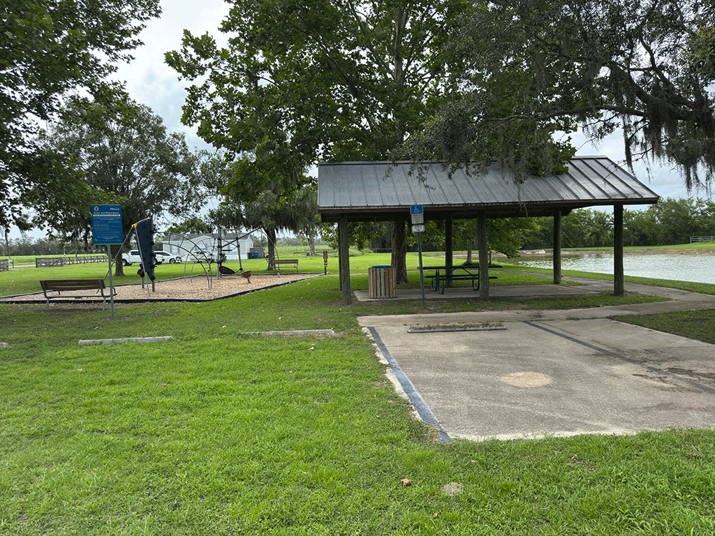 A playground and a covered picnic table by a pond.