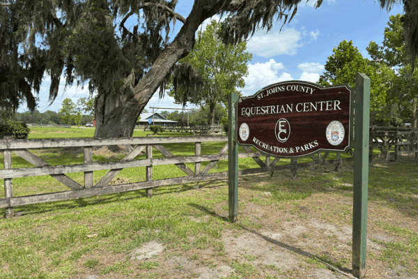 A sign for the St. Johns County Equestrian Center beside a fence and a large, picturesque tree.