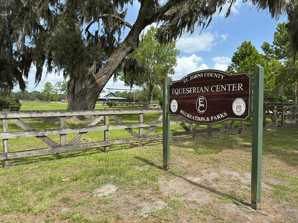 A sign for the St. Johns County Equestrian Center beside a fence and a large, picturesque tree.