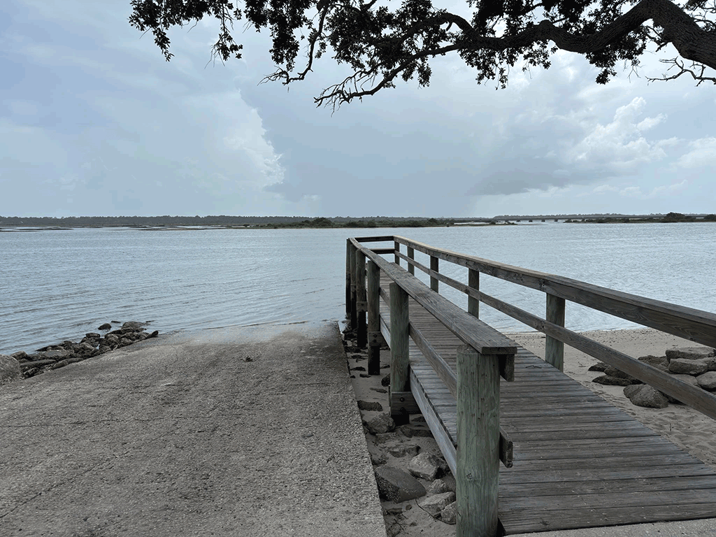 A concrete boat ramp next to a wooden fishing dock shaded by a tree