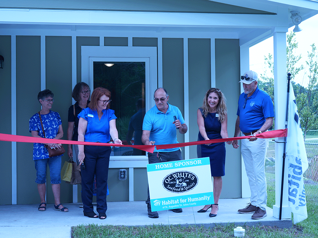 Commissioner Taylor and others cut a red ribbon in front of a home.