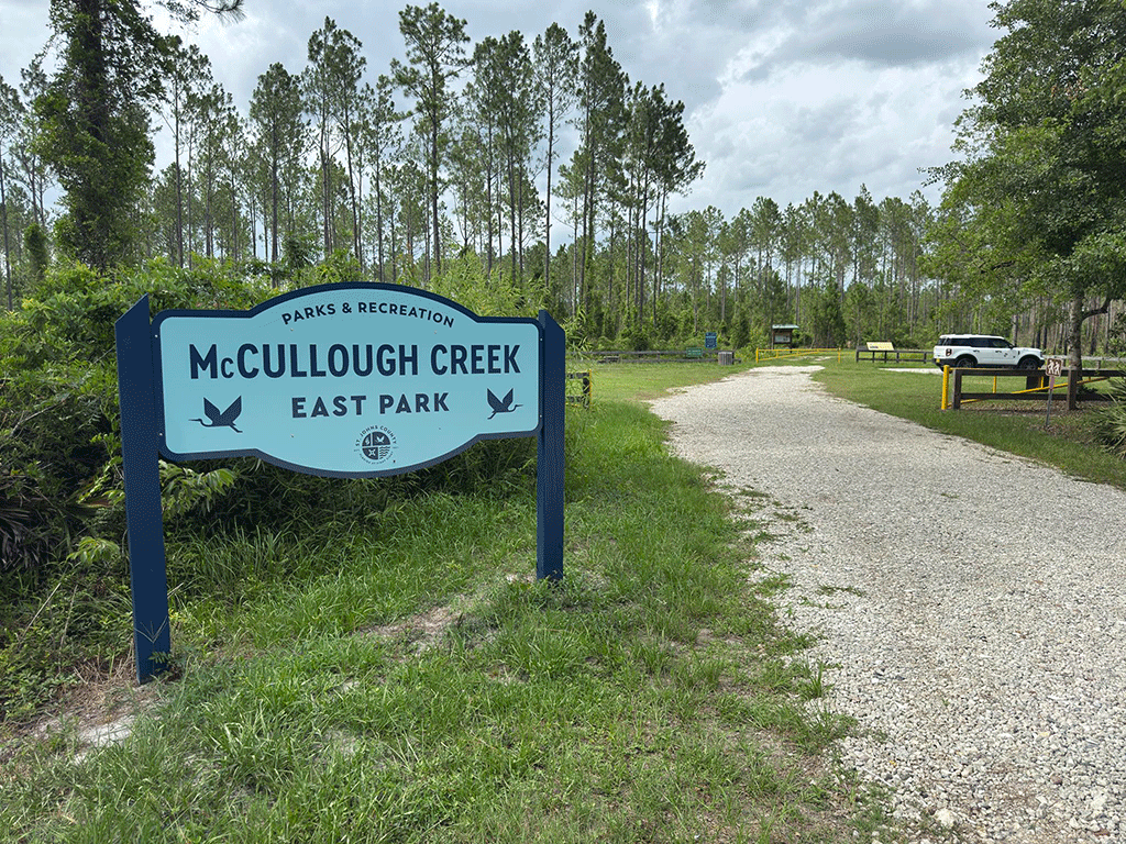 A sign detailing the history of the McCullough Creek area at the head of a trail into a wooded conservation area.