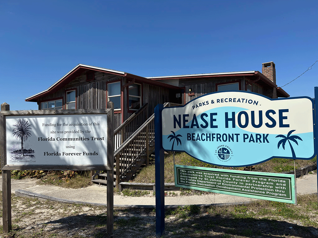 A sign for Nease Beachfront House in front of the house itself.