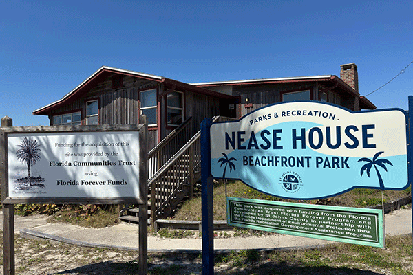 A sign for Nease Beachfront House in front of the house itself.